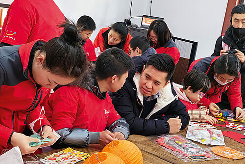 A group of young people in red shirts crafting lanterns sitting at a table.