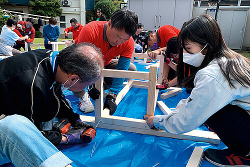 Photo: Hilti: Two older men and a young girl building a wooden construct using a HILTI drill.