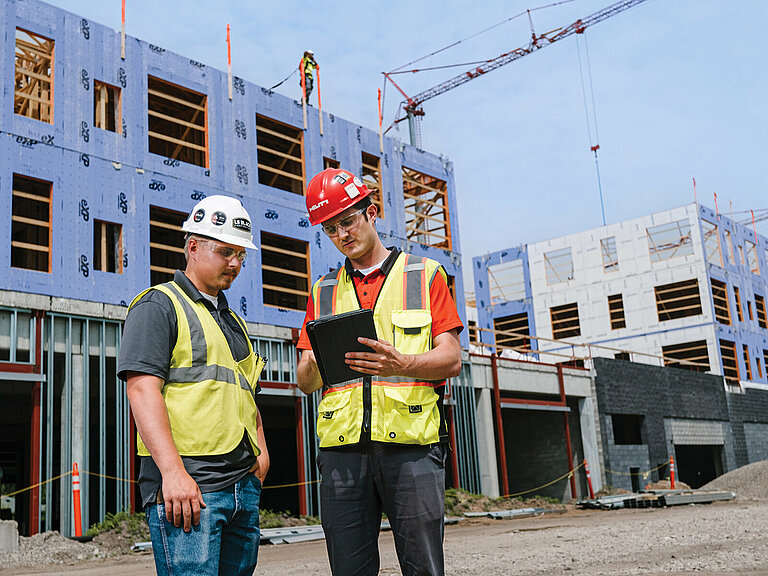 Photo: Hilti: Two workers with helmets are standing on the construction site looking at a tablet.