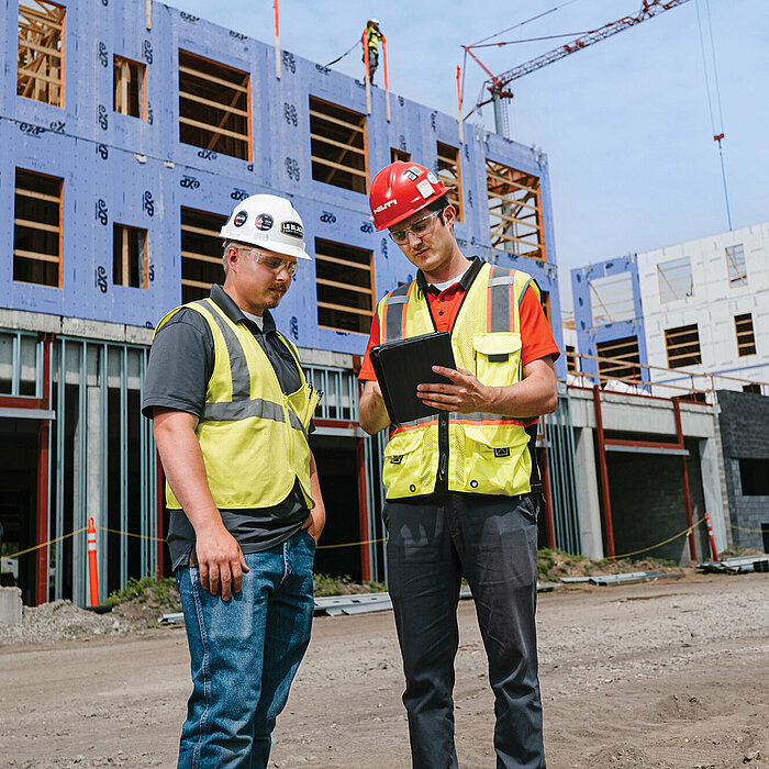 Photo: Hilti: Two workers with helmets are standing on the construction site looking at a tablet.