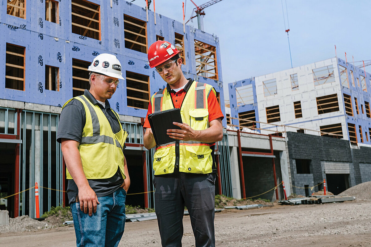 Photo: Hilti: Two workers with helmets are standing on the construction site looking at a tablet.