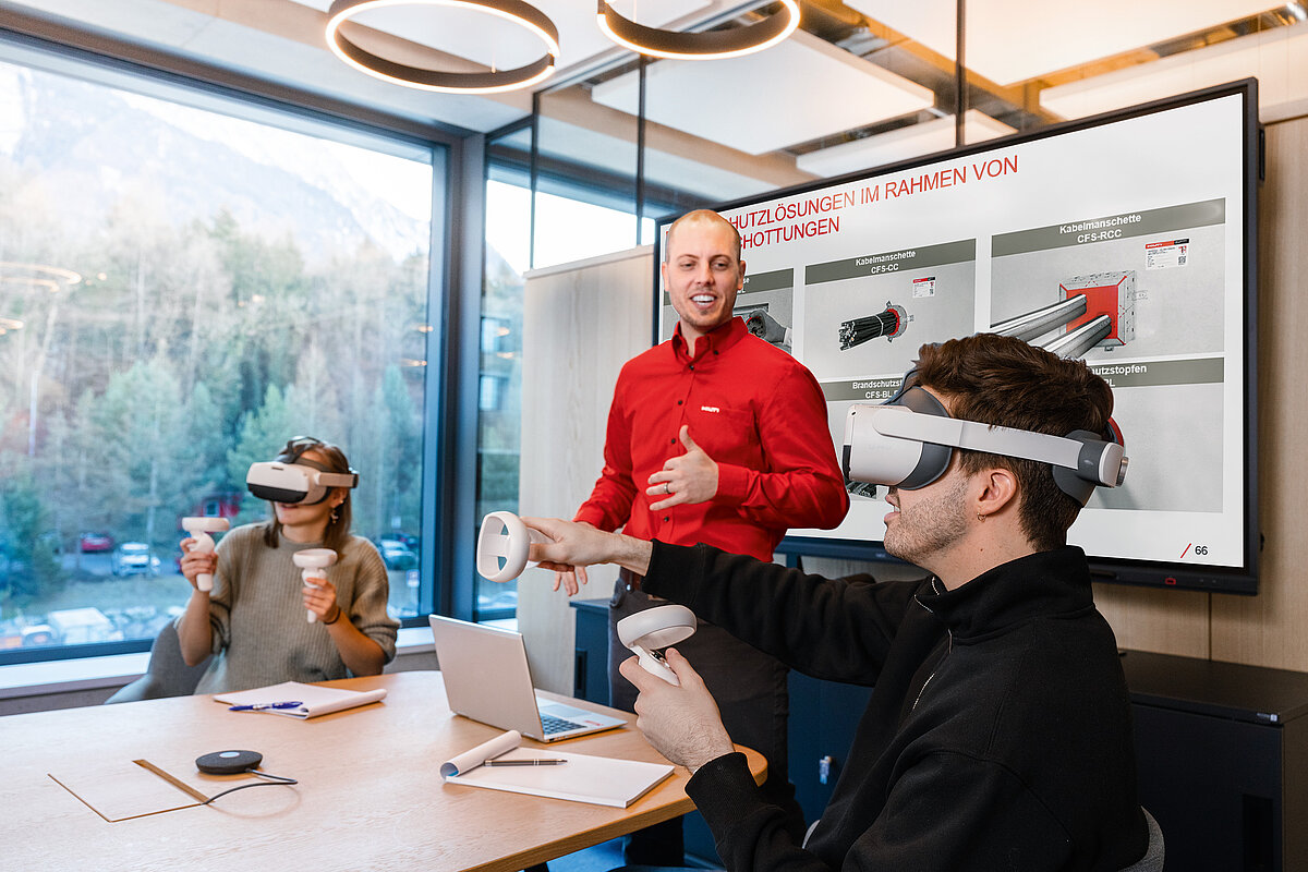 Photo: Hilti: 3 people in a room, sitting at a table. Two of them have virtual reality glasses on.