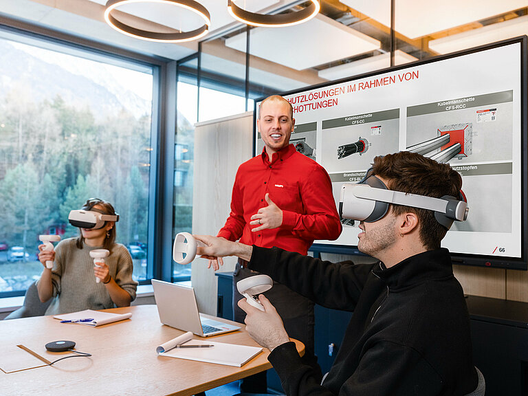 Photo: Hilti: 3 people in a room, sitting at a table. Two of them have virtual reality glasses on.