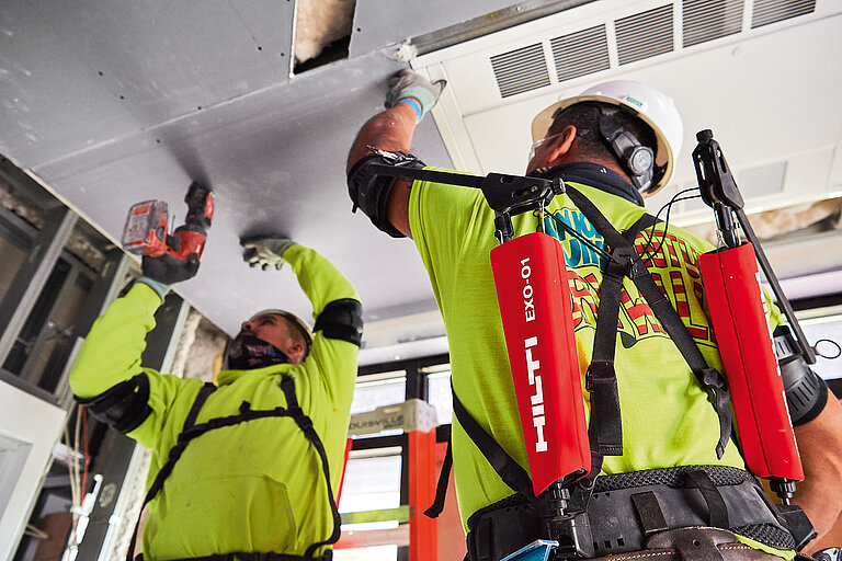 Photo: Hilti: 2 men with green shirts and white helmets working overhead with Hilti tools