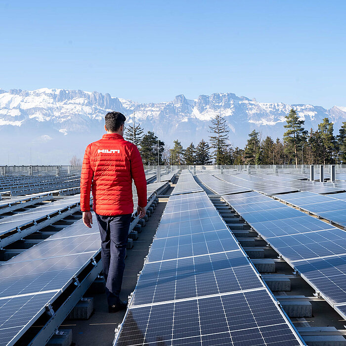 Photo: Hilti: Man from the back walking through solar panels, in the back there are mountains