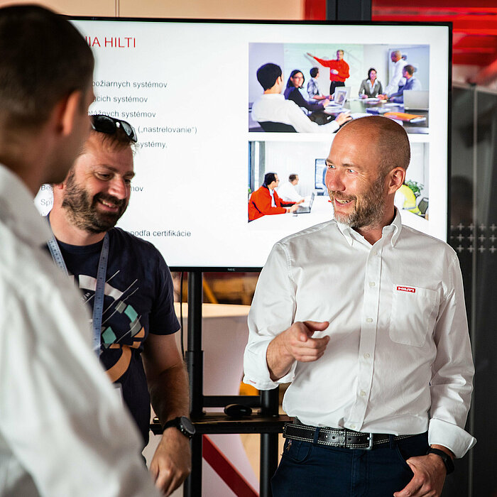 Photo: Hilti: 4 people standing in a room and talking, there is a big screen in the back