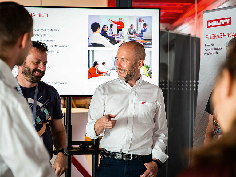 Photo: Hilti: 4 people standing in a room and talking, there is a big screen in the back