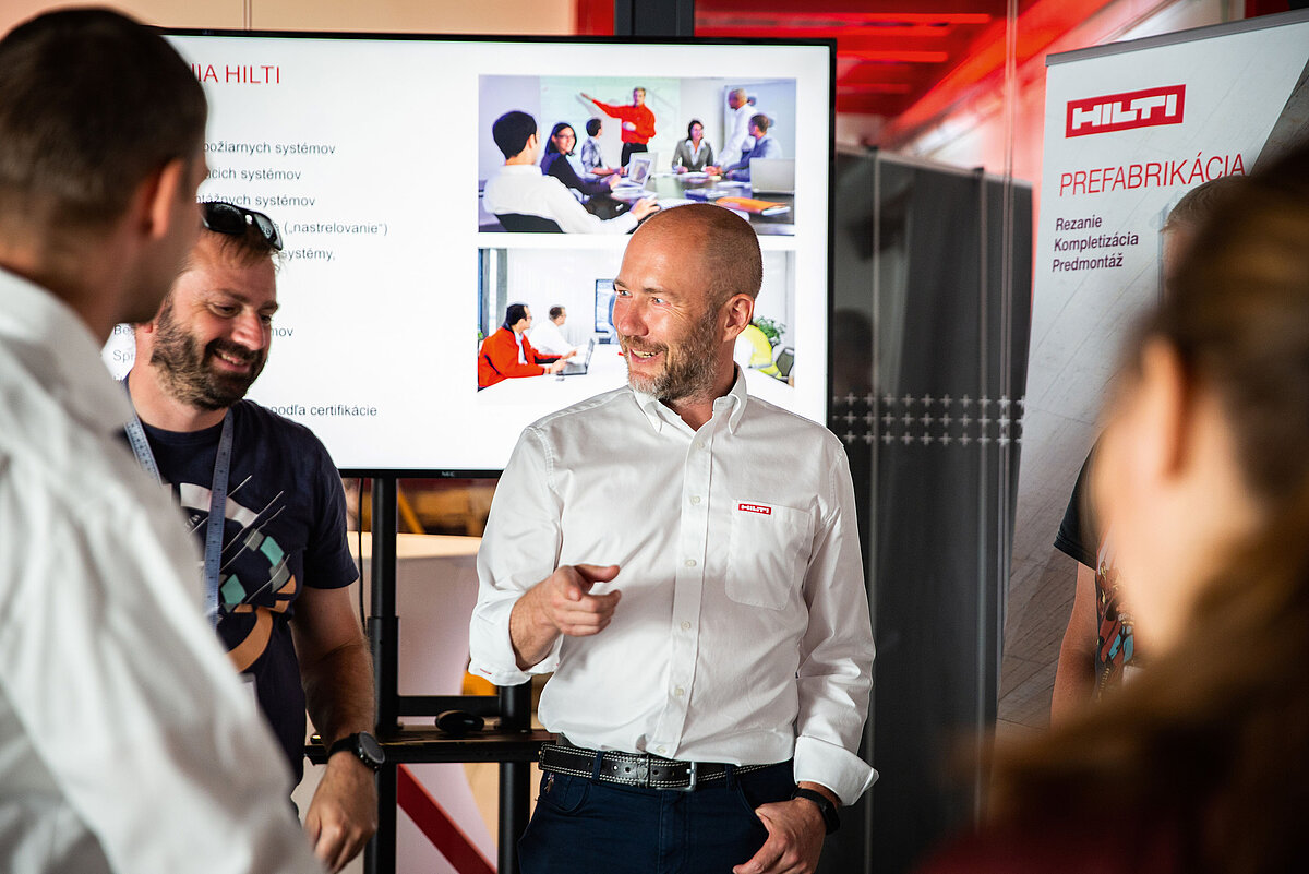 Photo: Hilti: 4 people standing in a room and talking, there is a big screen in the back
