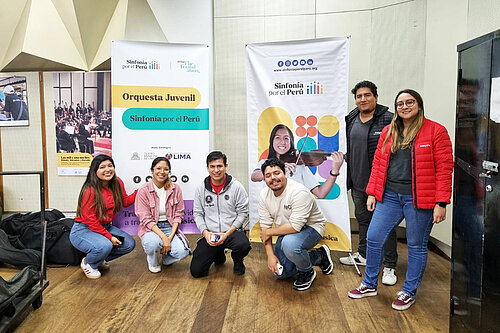Photo: Hilti: A group of Hilti Peru volunteers pose in front of two Sinfonía por el Perú banners, guitars in cases beside them