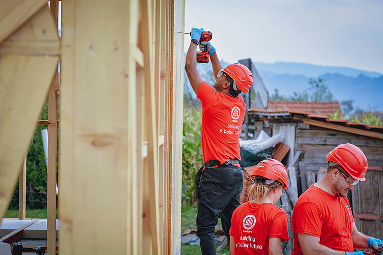 Three workers in Hilti-branded clothing stand next to a construction site. One of them is using a drill