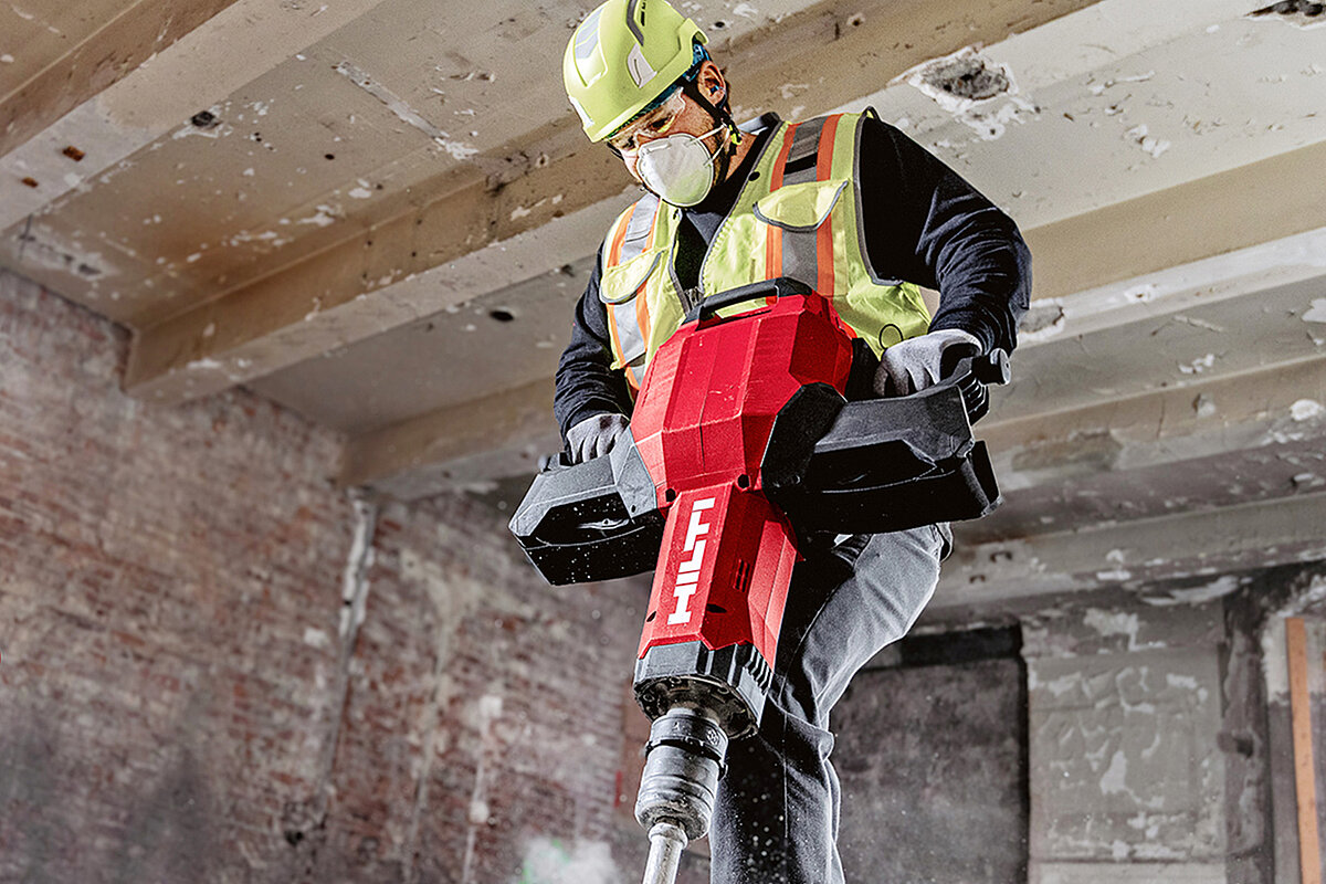 Hilti worker wearing a hard hat, safety glasses, and high-visibility vest while working with a Hilti tool on a construction site.