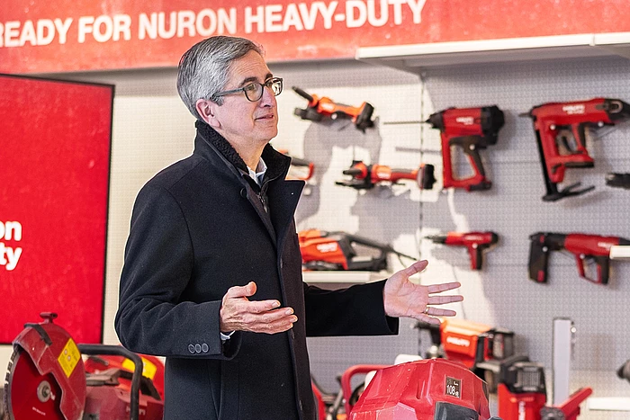 Profile of Jahangir Doongaji, CEO of Hilti, wearing a black coat, holding his palms open in an upward gesture. Various Hilti machines attached to a wall in the background.