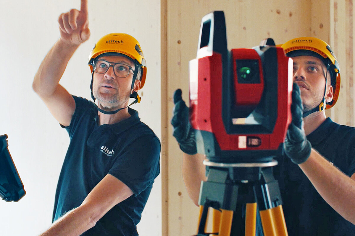 Two workers from Alltech Installation AG wearing yellow safety helmets and blue shirts, working together on the new construction of the Arlesheim Clinic near Basel.