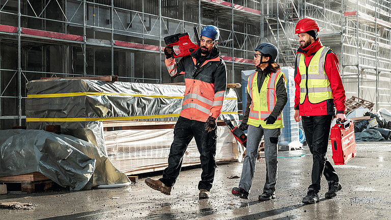 Hilti: Three construction workers, one woman and two men, wearing safety helmets and high-visibility vests, with Hilti tools in their hands. In the background, a construction site with scaffolding.