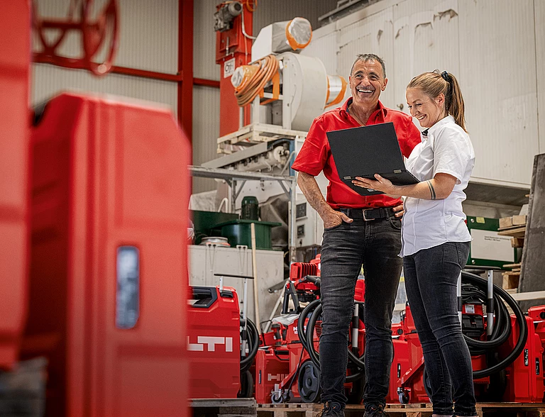 A salesperson holding a laptop next to a customer in a room full of Hilti tool cases