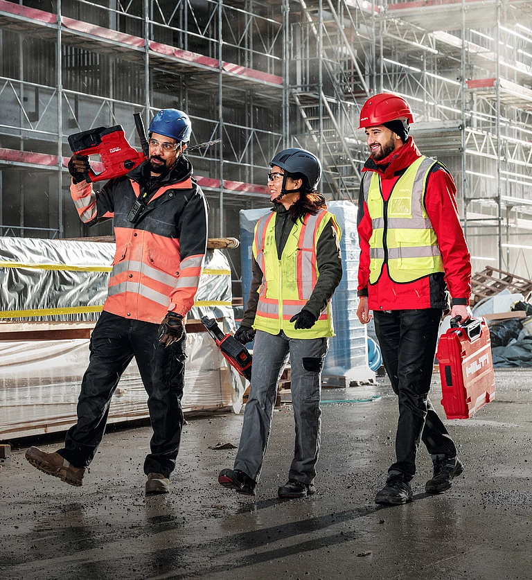 Hilti: Three construction workers, one woman and two men, wearing safety helmets and high-visibility vests, with Hilti tools in their hands. In the background, a construction site with scaffolding.