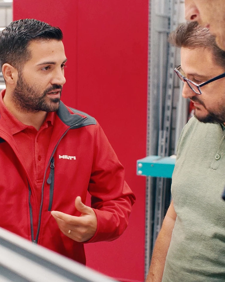 Three men, one wearing red Hilti clothing, in a planning meeting.
