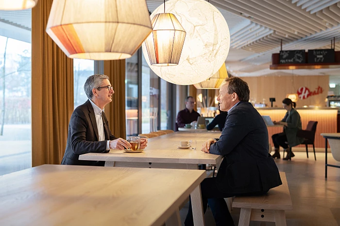 Profile of Hilti-CEO Jahangir Doongaji and Christoph Loos, Chairman of the Board of Directors, at a table in a restaurant while talking. Coffee and tea in front of them.