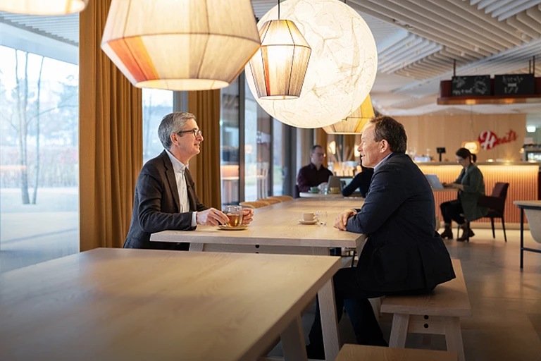 Hilti: CEO Jahangir Doongaji and Christoph Loos, Chairman of the Board of Directors, at a table in a restaurant while talking. Coffee and tea in front of them.